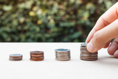 Cropped hand stacking coins on table against plants