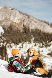 Dog and girl sitting on snow covered mountain