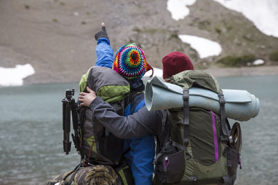 Rear view of hikers standing by lake against mountain during winter