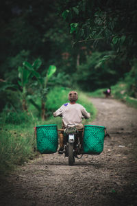 Rear view of man riding motorcycle with containers at field