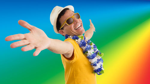 Portrait of excited man wearing sunglasses and floral garland while screaming against colored background