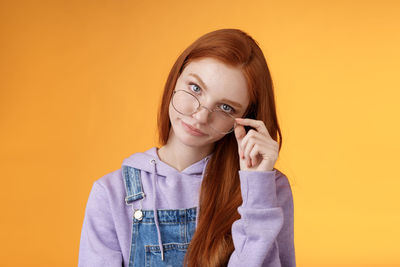 Serious woman holding sunglasses against yellow background