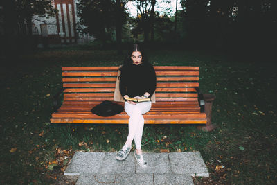 Portrait of young woman sitting on bench in park