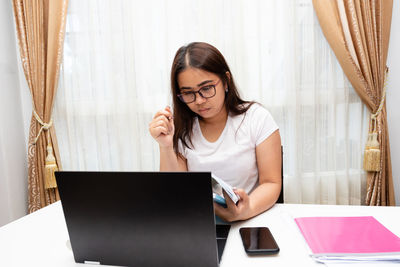 Young woman using phone while sitting on table