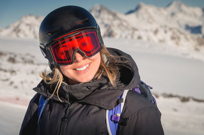 Skier smiles in a safety ski helmet and goggles against the backdrop of the picturesque alpine