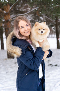 Young woman carrying dog while standing in snow during winter
