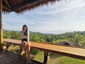 Woman sitting on bench against sky