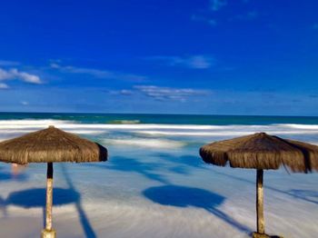 Thatched roof on shore at beach against blue sky