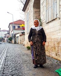 Full length portrait of woman standing on footpath against building