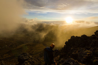 Man walking on mountain against sky during sunset