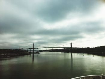 Suspension bridge over river against cloudy sky