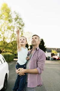 Son pointing up and showing to father while standing by car on street