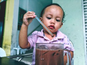 Cute baby boy holding straw in iced coffee at home