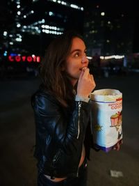 Young woman eating popcorn on street in city at night