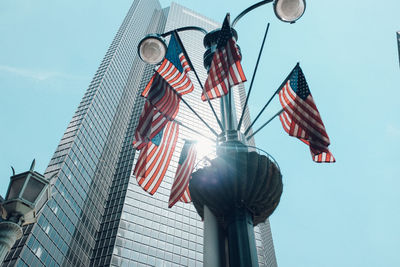 Low angle view of american flags by skyscraper against sky