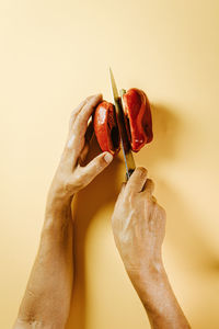 Cropped hands of woman cutting vegetable on beige background