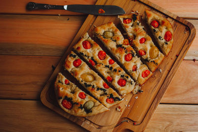 Homemade italian focaccia cut into slices, with tomato and olive oil on a rustic wooden background.