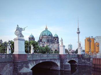 Sculptures on schlossbrucke bridge over spree river with berlin cathedral in background against sky