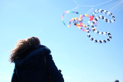 Low angle view of woman looking at snake kite flying against sky