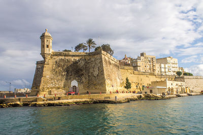 Buildings at waterfront against cloudy sky