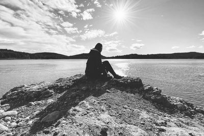 Man sitting on rock by lake against sky