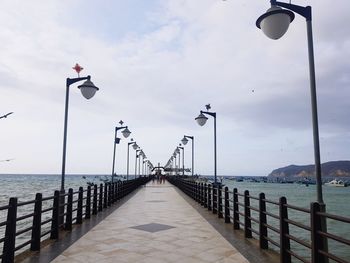 Street lights on pier by sea against sky