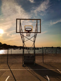 Basketball hoop on beach against sky during sunset