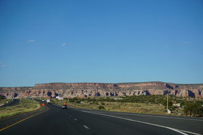 Road amidst grassy field against clear blue sky