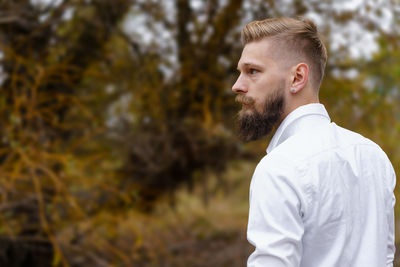 Young bearded man in white shirt walks on yellow autumn day in park. spending