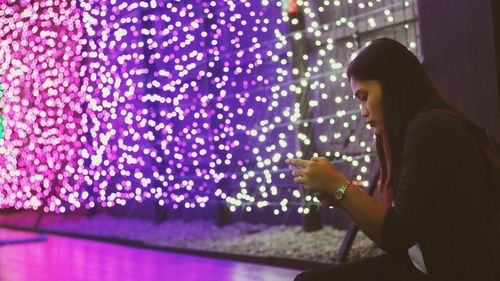 Side view of young woman using smart phone at night