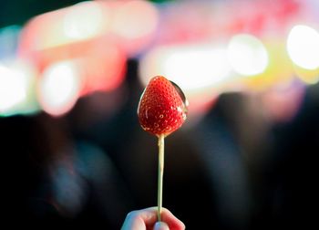 Close-up of hand holding strawberry lollipop at night