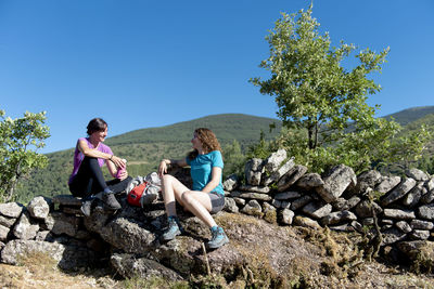 Two hiker girls resting and chating on a mountain path side.