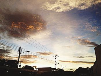 Low angle view of electricity pylon against cloudy sky