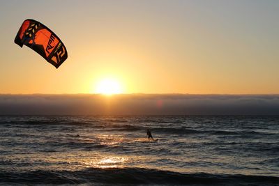 Man kiteboarding on sea against sky during sunset