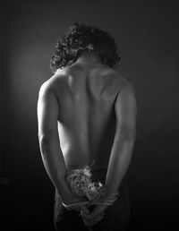 Rear view of shirtless woman with tied hands standing against wall