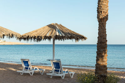 Deck chairs on beach against clear sky