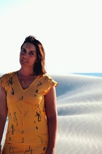 Portrait of young woman standing at beach against clear sky