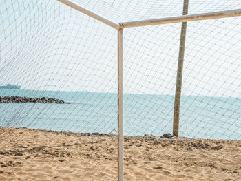 Close-up of chainlink fence on beach against sky