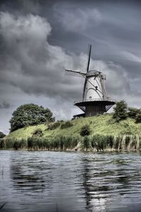 Traditional windmill by lake against sky