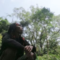 Side view of young man looking away against trees