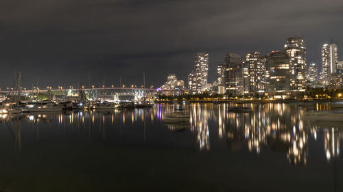 Illuminated buildings by sea against sky at night