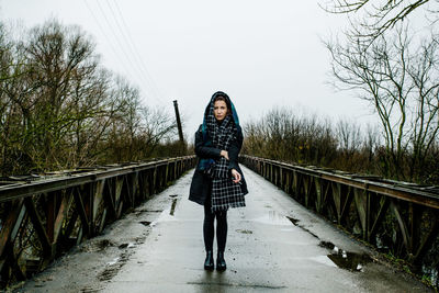 Full length portrait of young woman standing on footbridge