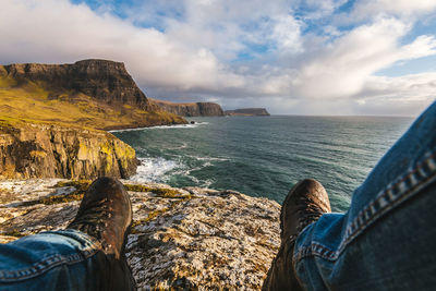 Low section of man on rock by sea against sky