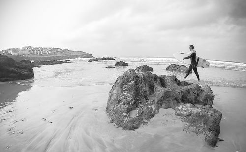 Man standing on rock at beach against sky