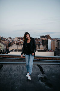 Full length portrait of young woman standing against sky in city