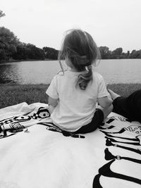 Rear view of woman relaxing by lake against sky