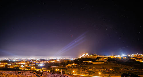 Illuminated buildings in town against sky at night