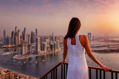 Rear view of woman standing against city during sunset