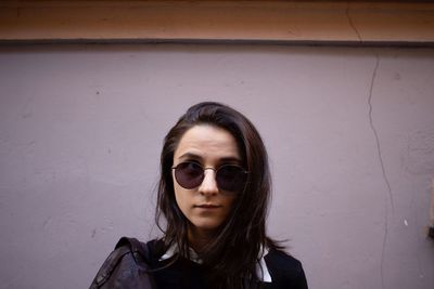 Portrait of young woman wearing sunglasses against wall