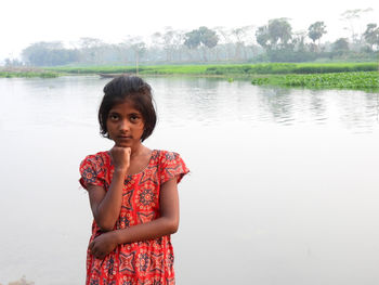 Portrait of young woman standing against lake